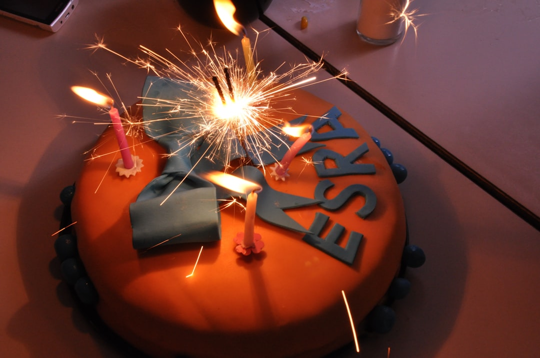 A beautifully decorated birthday cake with lit candles, surrounded by blurred party decorations and people celebrating.