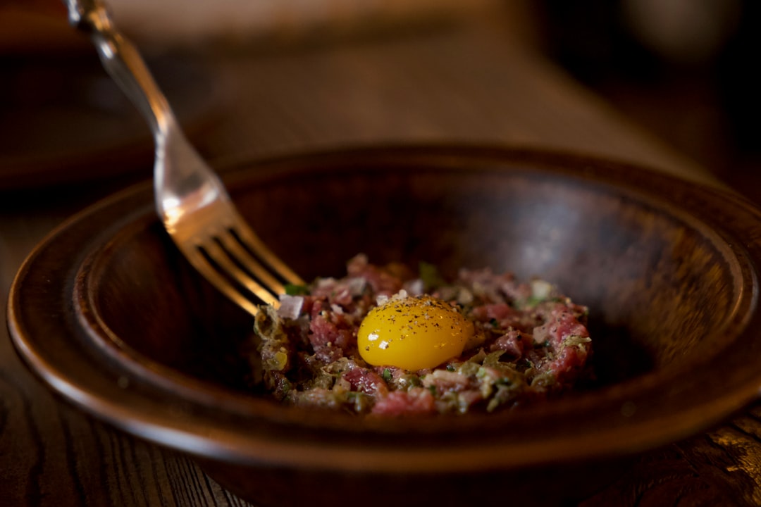 A close-up of a perfectly prepared Steak Tartare, with finely minced raw beef, capers, onions, and a vibrant raw egg yolk on top, served with toasted bread slices.