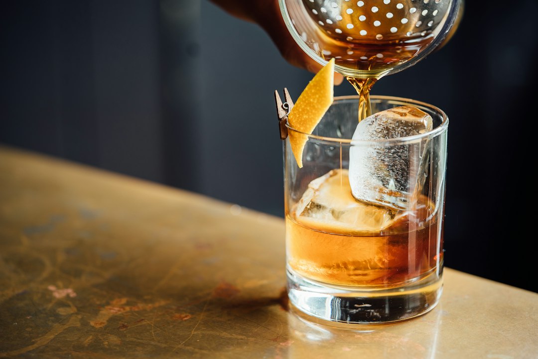 An Old Fashioned cocktail in a classic rocks glass with a large ice cube, orange peel, and a maraschino cherry